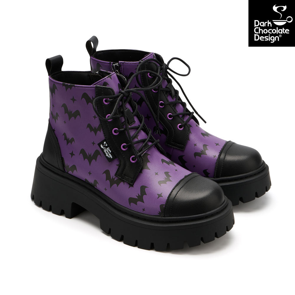 A pair of purple lace-up ankle boots with a black bat and star pattern, black leather toe caps and heel counters, and chunky black lug soles. A 'Dark Chocolate Design' brand logo is visible in the top right corner.