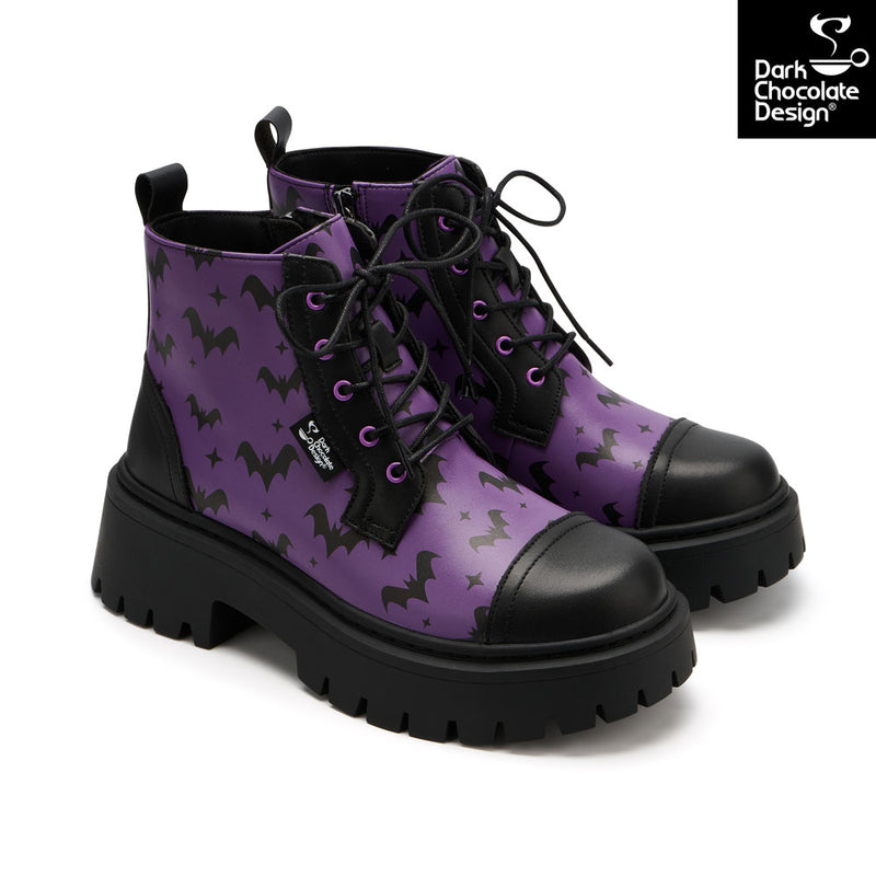 A pair of purple lace-up ankle boots with a black bat and star pattern, black leather toe caps and heel counters, and chunky black lug soles. A 'Dark Chocolate Design' brand logo is visible in the top right corner.